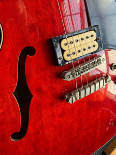 Red Ibanez hollowbody electric on the repair bench, bridge pickup and tailpiece in view