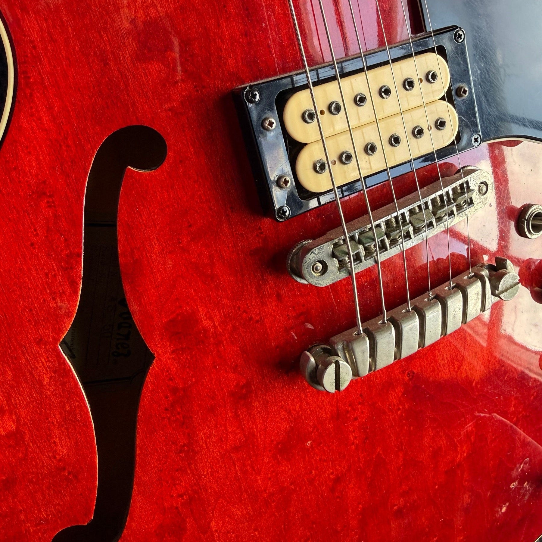 Red Ibanez hollowbody electric on the repair bench, bridge pickup and tailpiece in view