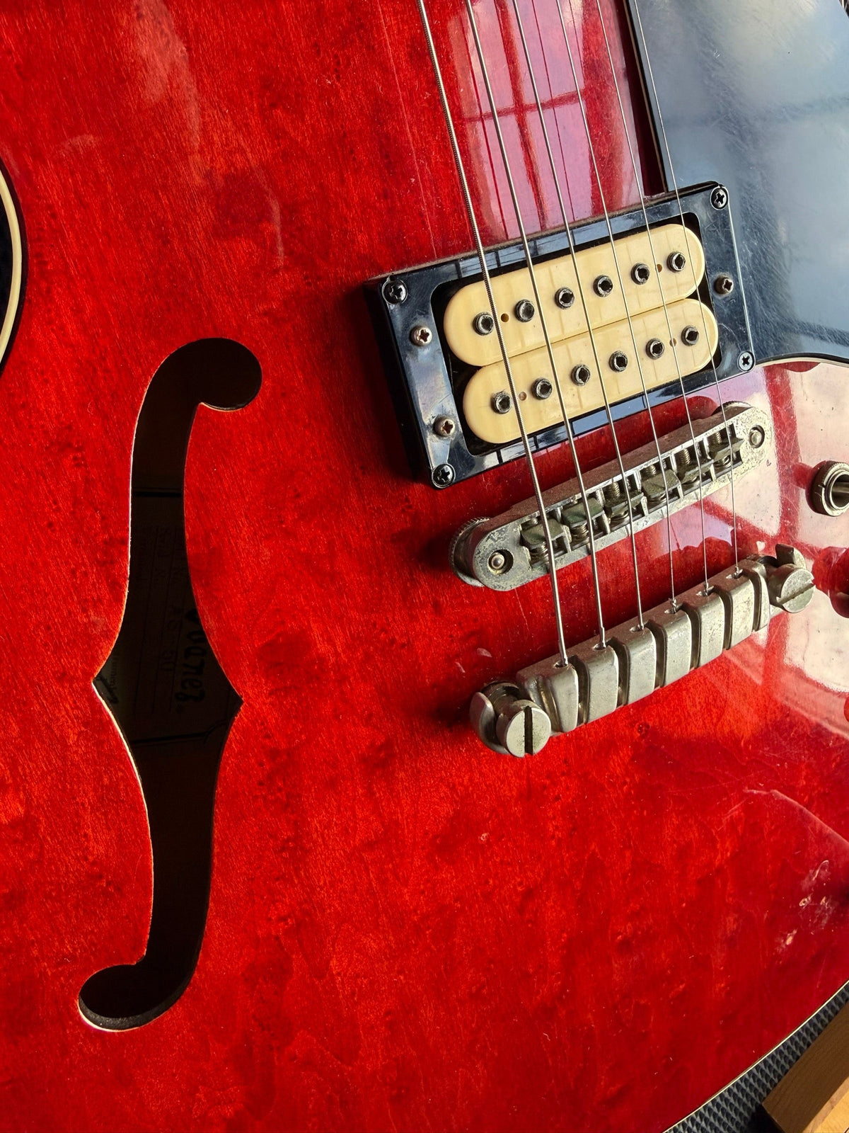 Red Ibanez hollowbody electric on the repair bench, bridge pickup and tailpiece in view
