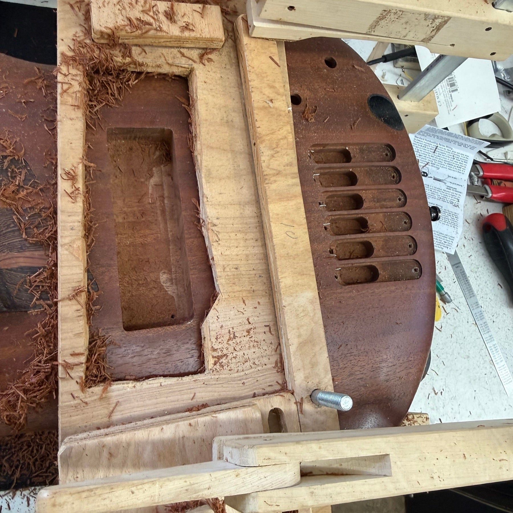 Ibanez SoundGear bass body clamped in a routing jig on the bench with one pickup cavity enlarged and shavings around it