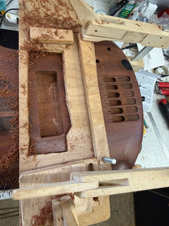 Ibanez SoundGear bass body clamped in a routing jig on the bench with one pickup cavity enlarged and shavings around it
