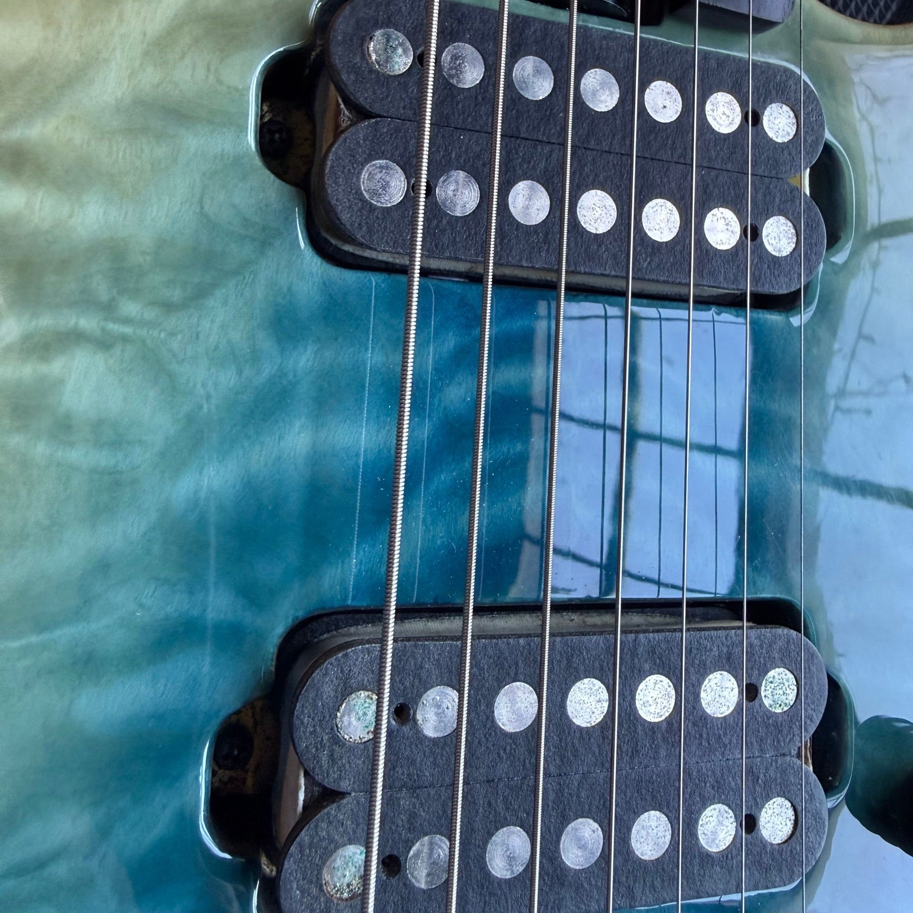 Schecter seven-string electric with a blue-green quilted top on the repair bench, both humbuckers visible