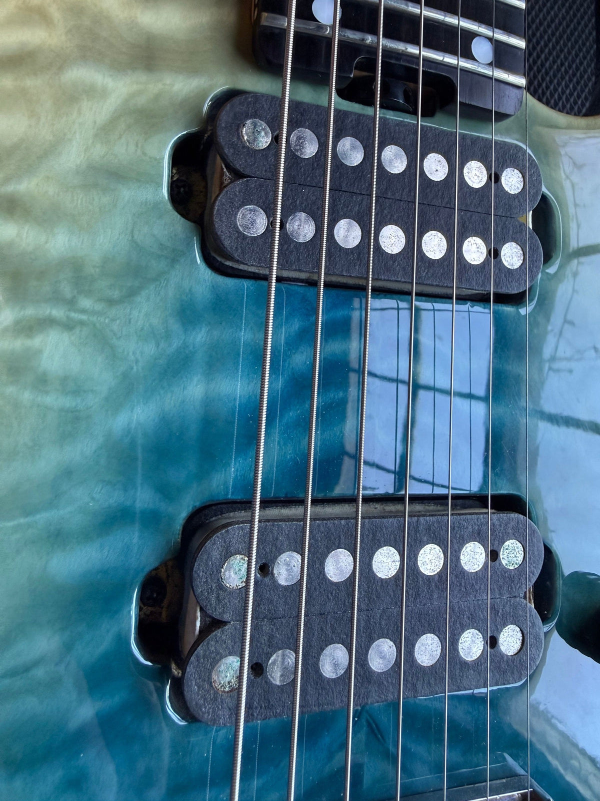 Schecter seven-string electric with a blue-green quilted top on the repair bench, both humbuckers visible
