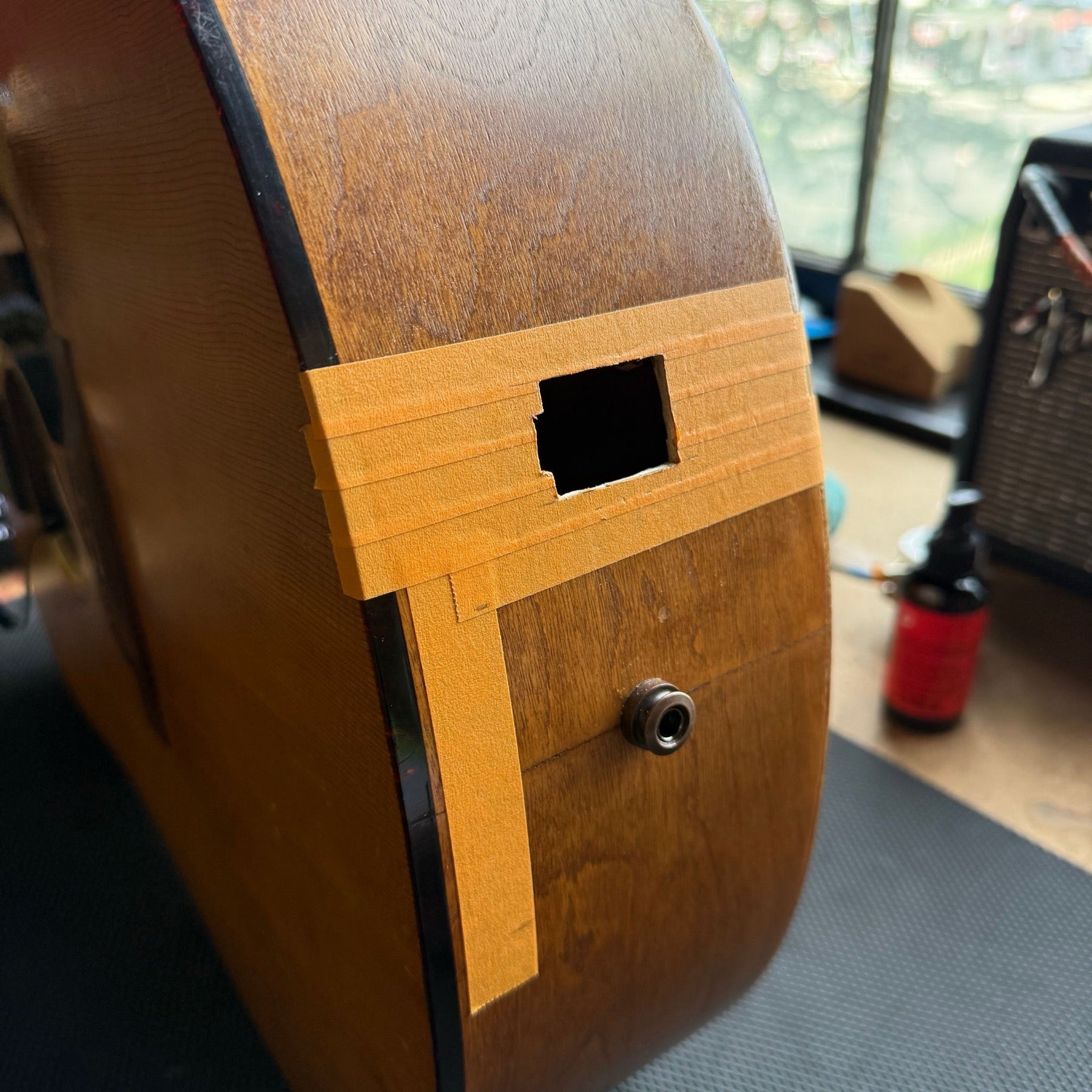 Side of a Seagull dreadnought on the repair bench with the battery box opening cut and taped, endpin jack below it