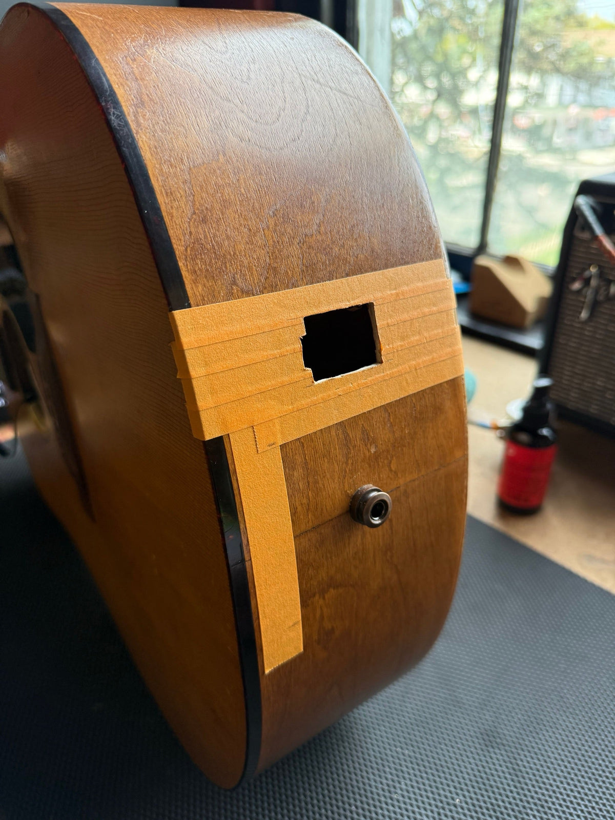 Side of a Seagull dreadnought on the repair bench with the battery box opening cut and taped, endpin jack below it