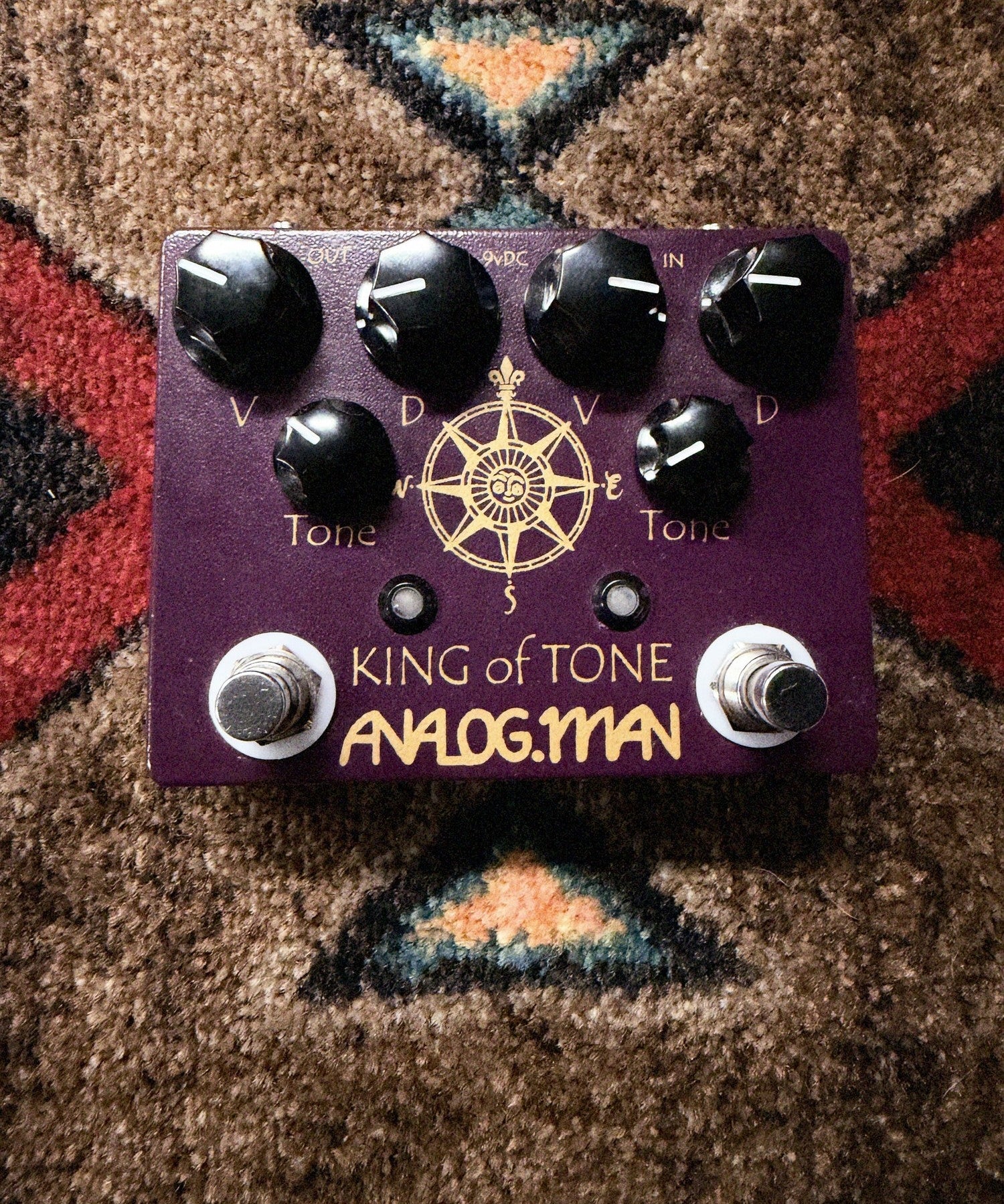 Analogman King of Tone V4, purple: top with the Volume, Drive and Tone knobs for each side, two footswitches and the gold compass graphic