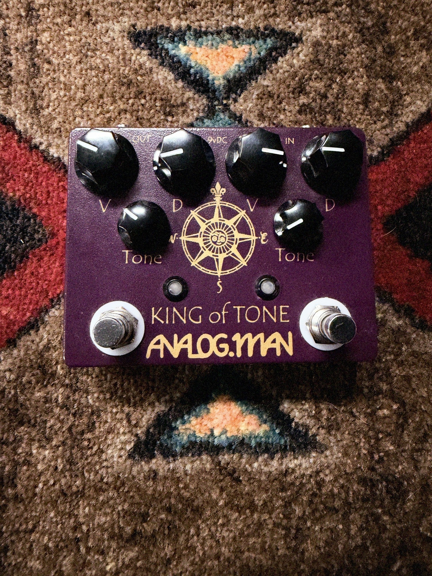 Analogman King of Tone V4, purple: top with the Volume, Drive and Tone knobs for each side, two footswitches and the gold compass graphic