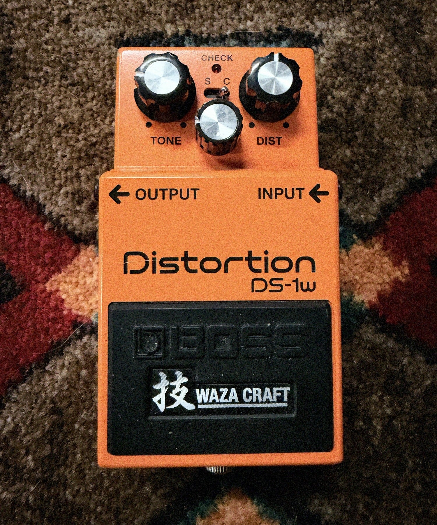 Boss DS-1W Waza Craft Distortion, orange: top with the Tone, Level and Dist knobs, the S and C mode switch, the Check light and the Waza Craft pedal