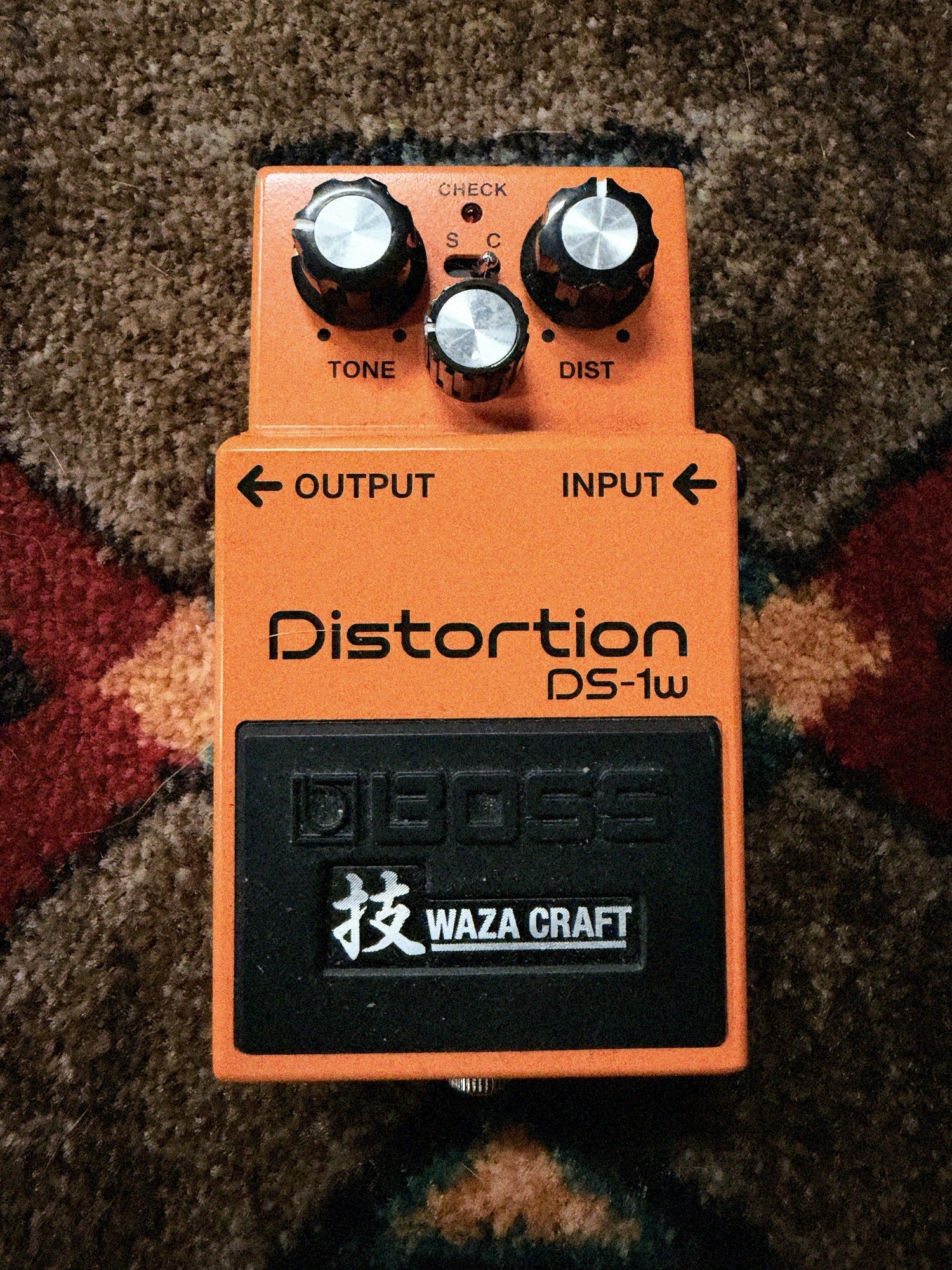 Boss DS-1W Waza Craft Distortion, orange: top with the Tone, Level and Dist knobs, the S and C mode switch, the Check light and the Waza Craft pedal