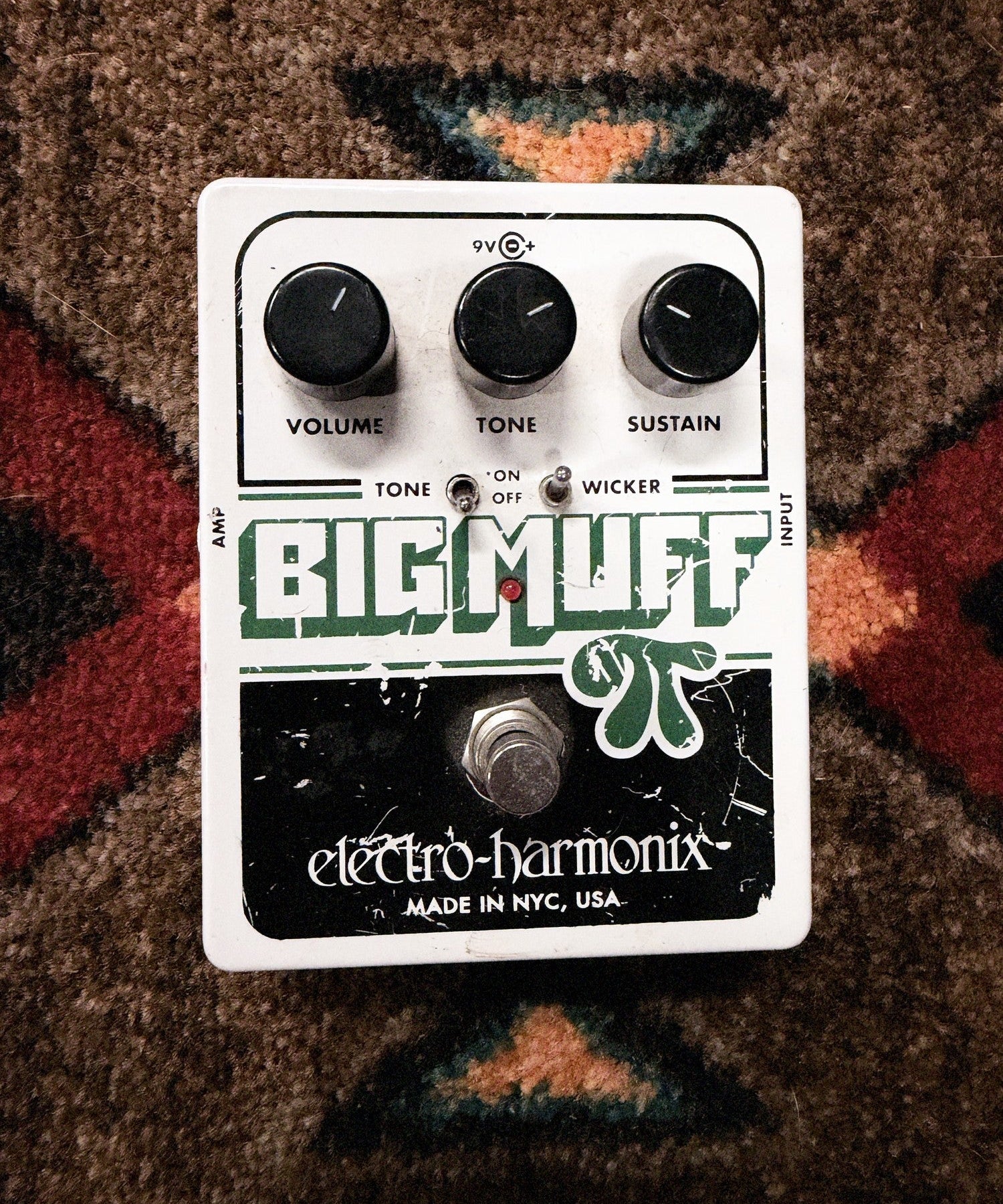 Electro-Harmonix Big Muff Pi with Tone Wicker, white: top with the Volume, Tone and Sustain knobs, the Tone and Wicker switches and the footswitch, with scratches and chips in the green and black print