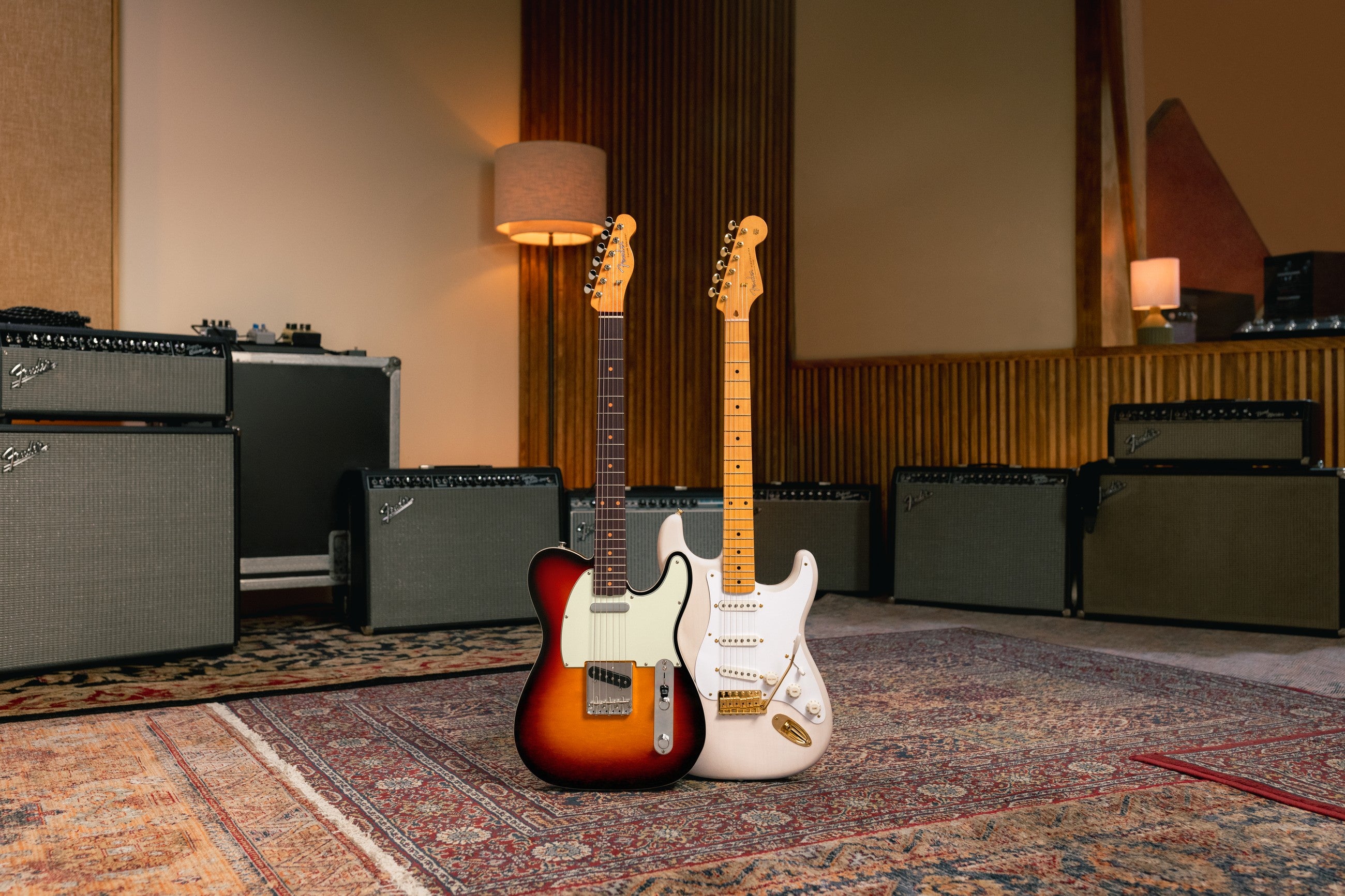 A Fender Telecaster and Stratocaster on a stand in a warm studio with amps and amber light. Guitar lessons at Paul's Guitar Hideout.