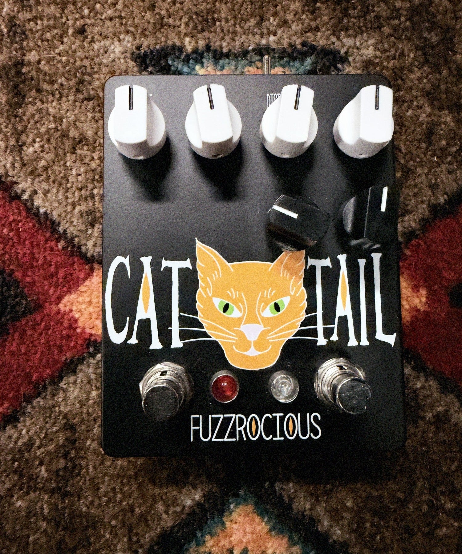 Fuzzrocious Cat Tail with 2nd Distortion Mod, black: top with the orange cat graphic, four white knobs, two black clipping knobs, two footswitches and the red and clear LEDs