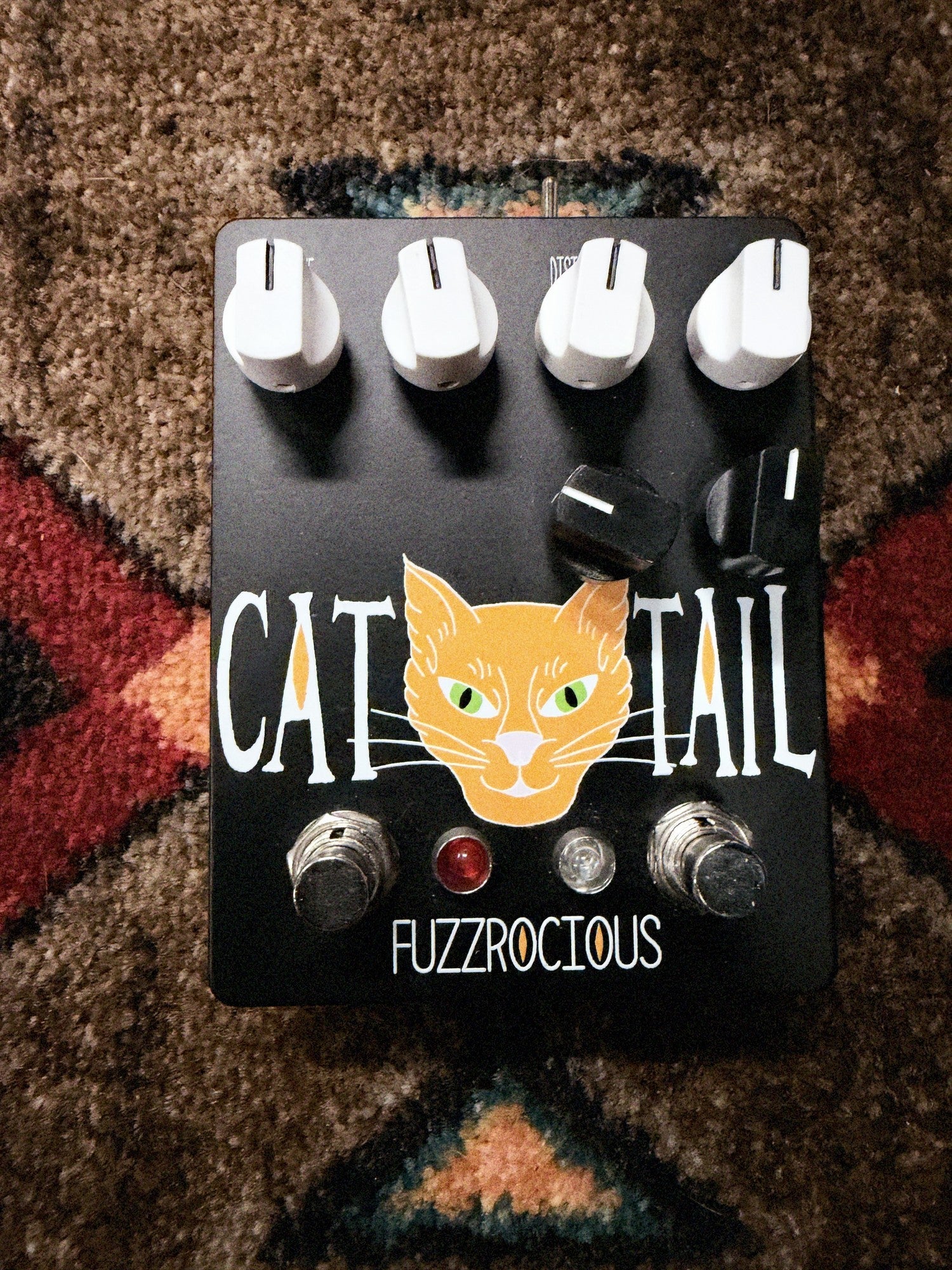 Fuzzrocious Cat Tail with 2nd Distortion Mod, black: top with the orange cat graphic, four white knobs, two black clipping knobs, two footswitches and the red and clear LEDs