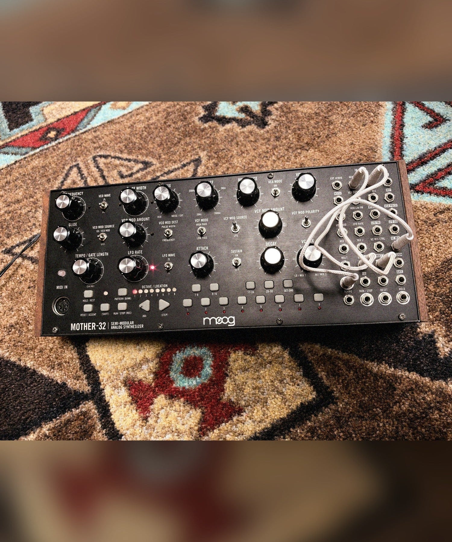 Moog Mother-32, black: the panel from above with white patch cables in the patch bay and wood end cheeks