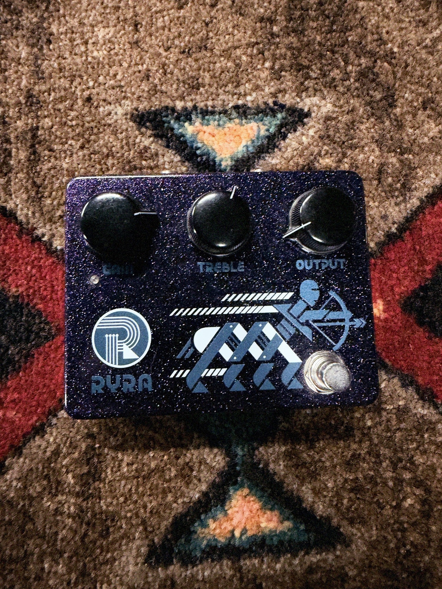 RYRA The Klone, dark blue sparkle: top with the Gain, Treble and Output knobs, the RYRA logo, the archer graphic and the footswitch