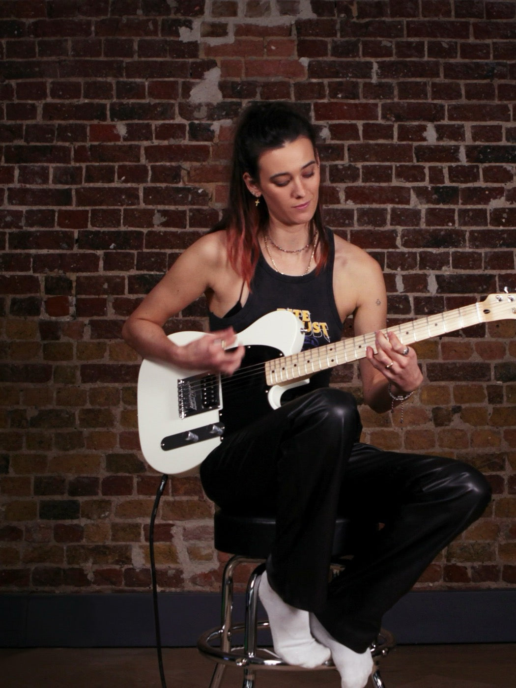 Beginner guitar lesson — playing a Squier against a brick wall